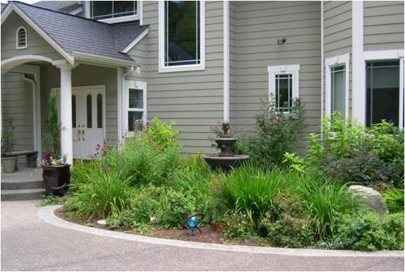 Front yard of a grey house with white trim, landscaped garden, green plants, and a small fountain near the entryway.