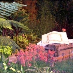 A stone bench surrounded by pink flowers and lush greenery in a garden setting.