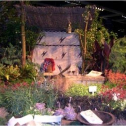 Garden display with tropical plants, a thatched backdrop, a flag, and various artifacts arranged on the ground.